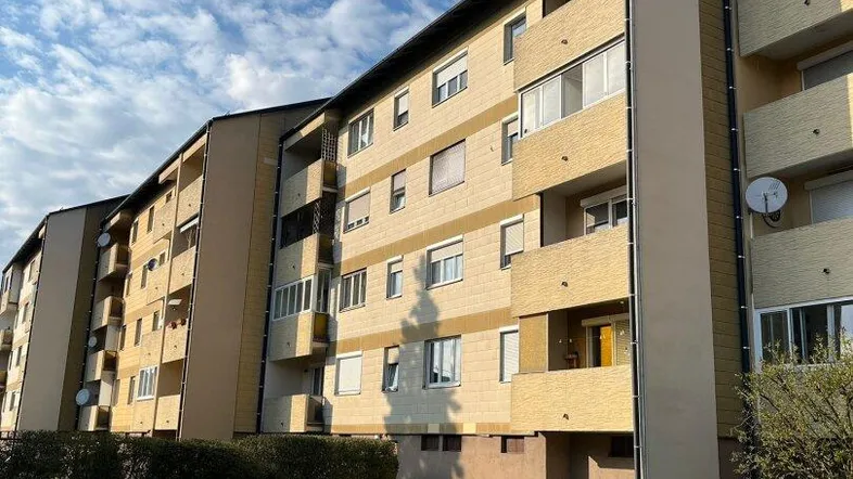 Mehrfamilienhaus mit mehreren Etagen und Balkonen, umgeben von einer gepflegten Grünfläche unter blauem Himmel.