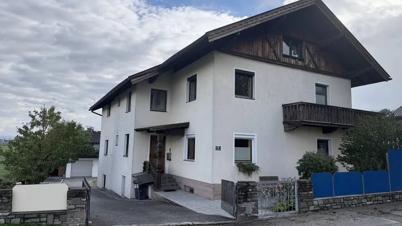 Traditionelles Wohnhaus mit weißer Fassade, Holzbalkonen und Satteldach in ländlicher Umgebung.