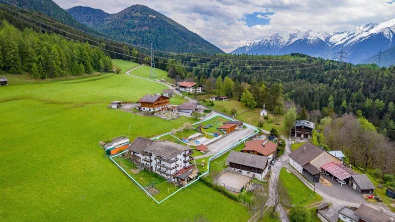 Luftaufnahme eines Anwesens in einer malerischen alpinen Landschaft mit grünen Wiesen und schneebedeckten Bergen.