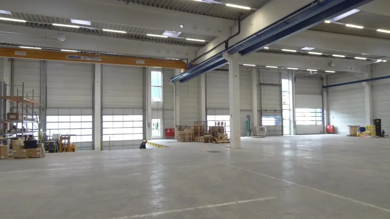 Geräumige Lagerhalle mit hohen Decken, Betonboden und mehreren Rolltoren für den Zugang und Tageslicht.