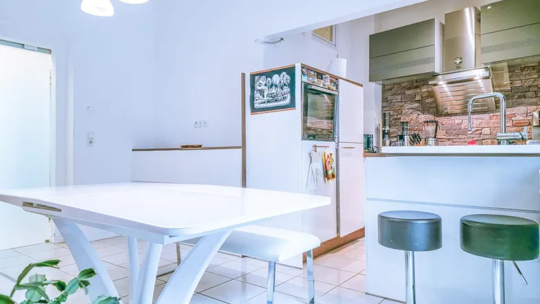 Moderne Küche mit weißem Esstisch, Barhockern und integrierten Geräten.