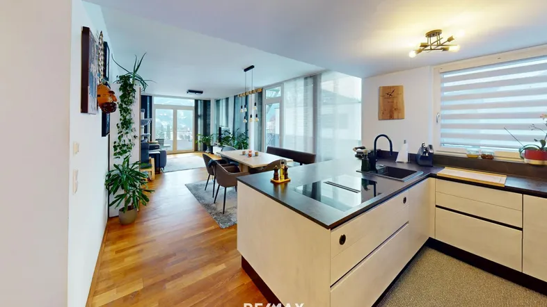 Moderner offener Wohn-Essbereich mit integrierter Küche, Holzboden und Zugang zum Balkon.