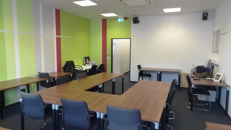 Geräumiger Konferenzraum mit mehreren Tischen und Stühlen, ideal für Besprechungen oder Schulungen.