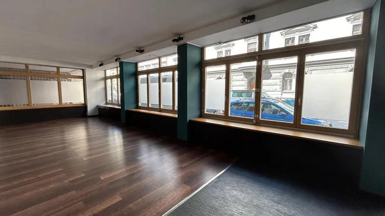 Geräumiger, leerer Gewerberaum mit großen Fenstern und dunklem Laminatboden, ideal für Laden oder Büro.