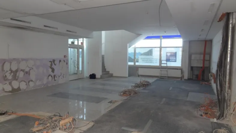 Großer, heller Gewerberaum im Rohbauzustand mit sichtbaren Installationen und großen Fenstern, bereit für den Ausbau.
