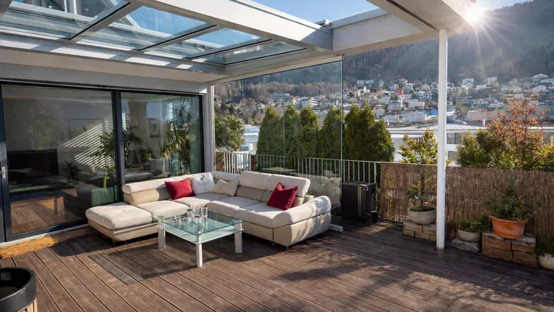 Große, sonnige Terrasse mit bequemen Loungemöbeln, Glasdach und weitem Blick über die Stadt und Hügel.