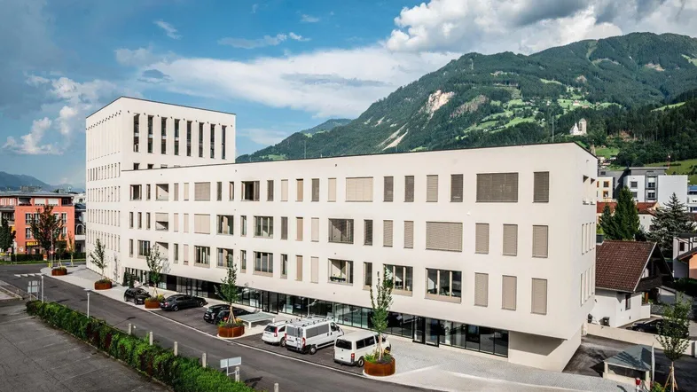 Modernes, weißes Geschäftsgebäude mit großen Fenstern und beeindruckendem Bergblick unter blauem Himmel.