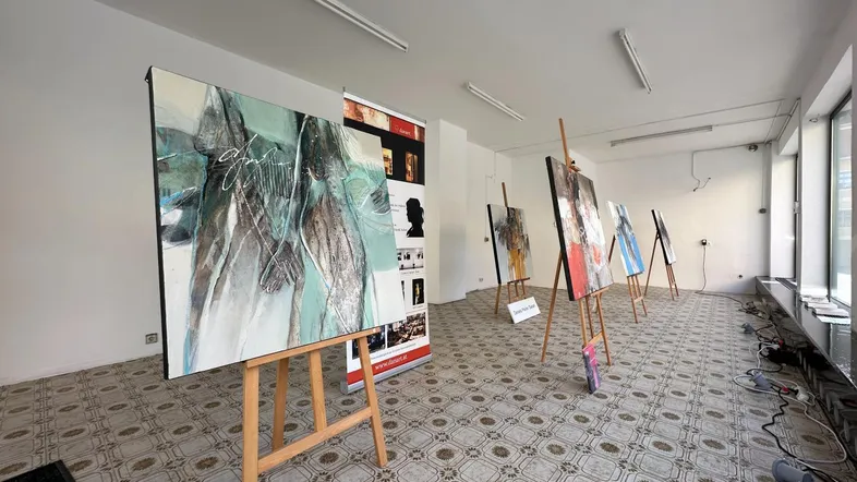 Heller Ausstellungsraum mit Kunstwerken auf Staffeleien und gemustertem Fliesenboden, ideal für Präsentationen.