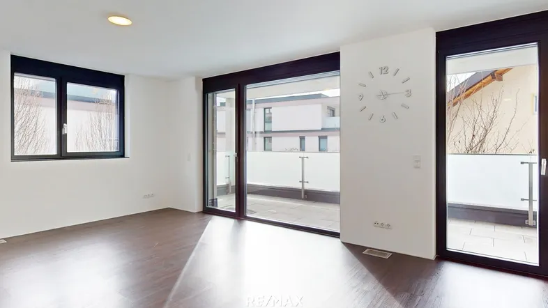 Helles, leeres Zimmer mit dunklem Holzboden und Zugang zu einem Balkon.