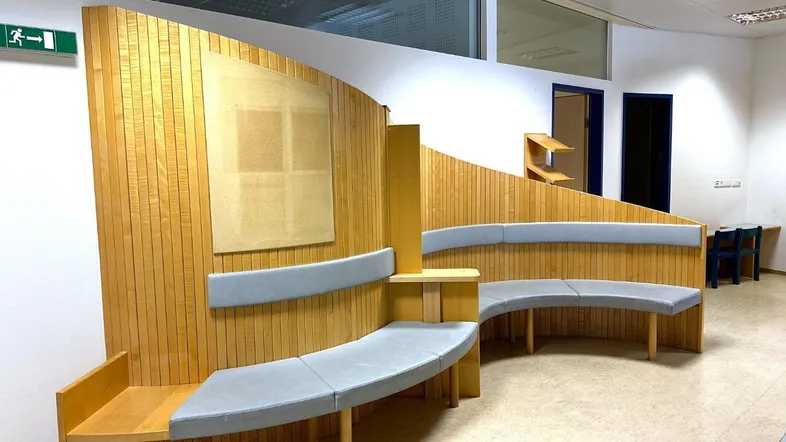Geschwungene Sitzbank mit Holzvertäfelung und Polstern in einem Wartebereich.