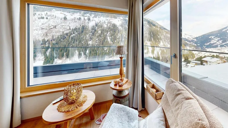 Gemütlicher Wohnbereich mit großen Fenstern und atemberaubendem Blick auf die verschneiten Berge.