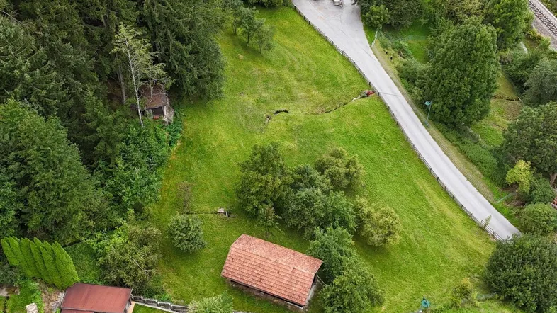 Luftaufnahme eines grünen, hügeligen Grundstücks mit Bäumen und einer kurvigen Straße.