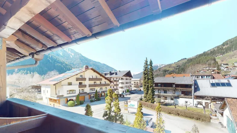 Blick vom Balkon auf ein malerisches Bergdorf mit traditionellen Häusern und grünen Hängen.