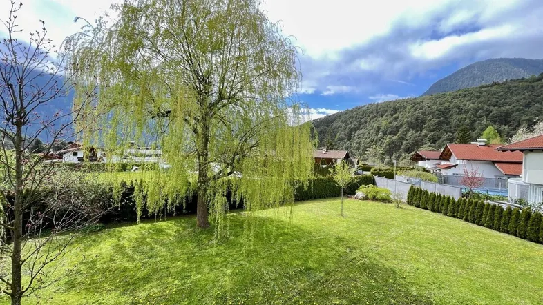 Großer Garten mit Rasenfläche, altem Baum und weitem Blick auf die umliegende Berglandschaft.
