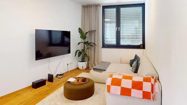 Helles Wohnzimmer mit bequemer Couch, Holzboden und einem großen Fenster, das viel Tageslicht hereinlässt.