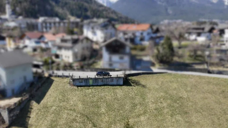 Luftaufnahme eines Grundstücks mit einem Auto und Blick auf ein Dorf und die umliegenden Berge.