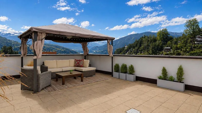 Geräumige Dachterrasse mit gemütlicher Lounge-Ecke, Pavillon und atemberaubendem Bergblick unter blauem Himmel.