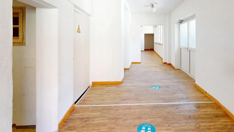 Langer, heller Flur mit Holzboden und weißen Wänden, ideal für Büroräume oder Gewerbeflächen.