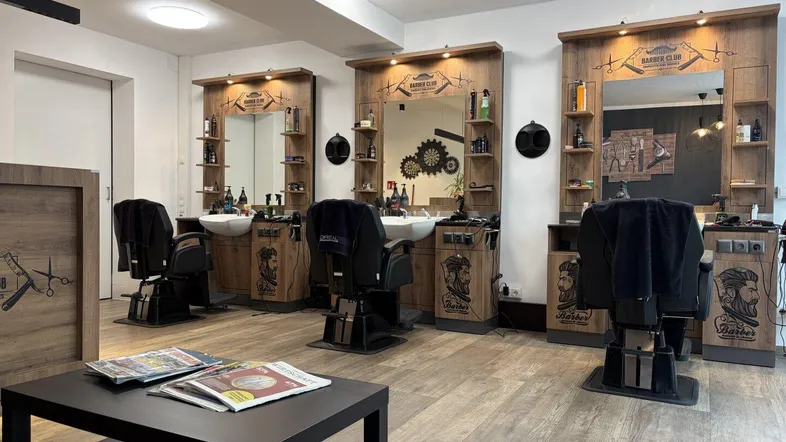 Heller Friseursalon mit drei modernen Bedienplätzen, Holzvertäfelung und einem kleinen Wartebereich.