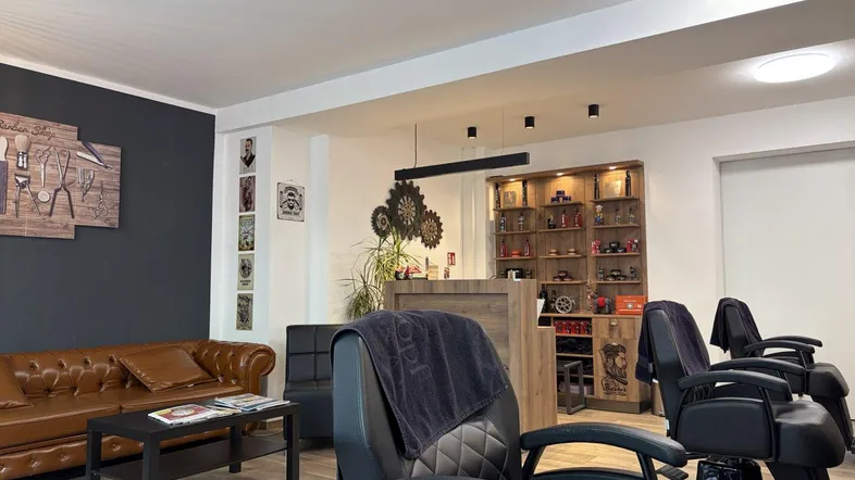 Empfangsbereich eines Friseursalons mit bequemer Ledercouch, Rezeption und weiteren Arbeitsplätzen.