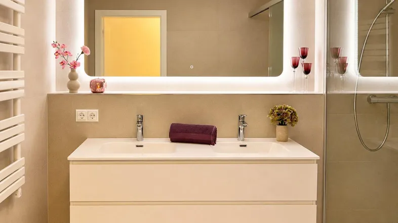 Modernes Badezimmer mit Doppelwaschbecken, beleuchtetem Spiegel und einer geräumigen begehbaren Dusche.