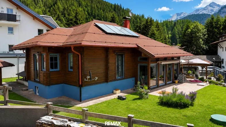 Charmantes Holzhaus mit rotem Dach, Solarpaneelen und gepflegtem Garten in alpiner Umgebung.