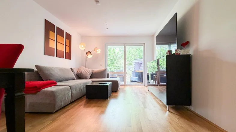 Gemütliches Wohnzimmer mit großem Sofa, Holzboden und Zugang zu einem sonnigen Balkon.