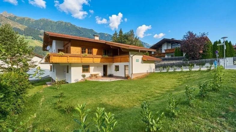 Traditionelles Haus im alpinen Stil mit Holzbalkonen und Bergblick unter blauem Himmel.