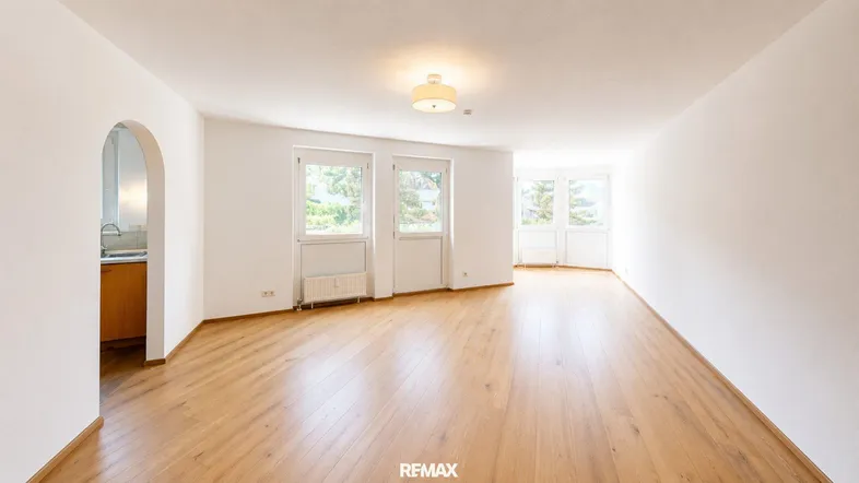 Helles, leeres Wohnzimmer mit Parkettboden und mehreren Fenstern, das viel Tageslicht bietet.