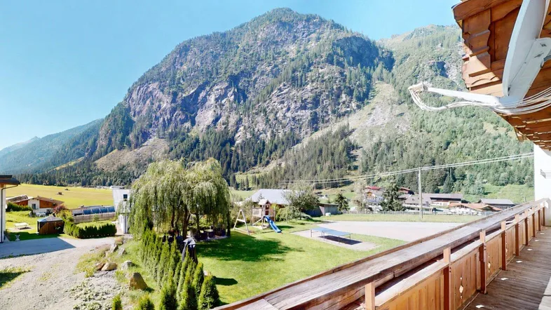Geräumiger Holzbalkon mit weitem Blick auf die umliegende Berglandschaft und einen Spielplatz.