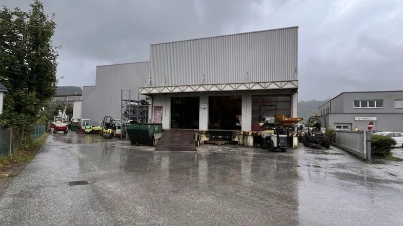 Außenansicht eines Industriegebäudes mit Laderampe und asphaltiertem Vorplatz unter bewölktem Himmel.