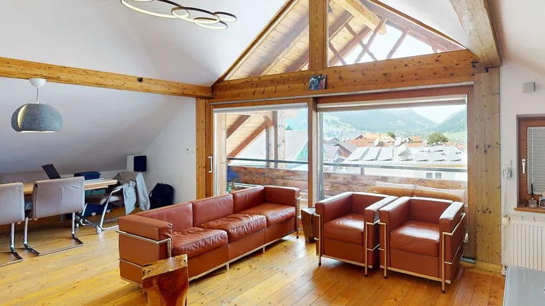 Helles Wohnzimmer mit Holzbalken, großen Fenstern und Bergblick in einem Dachgeschoss.