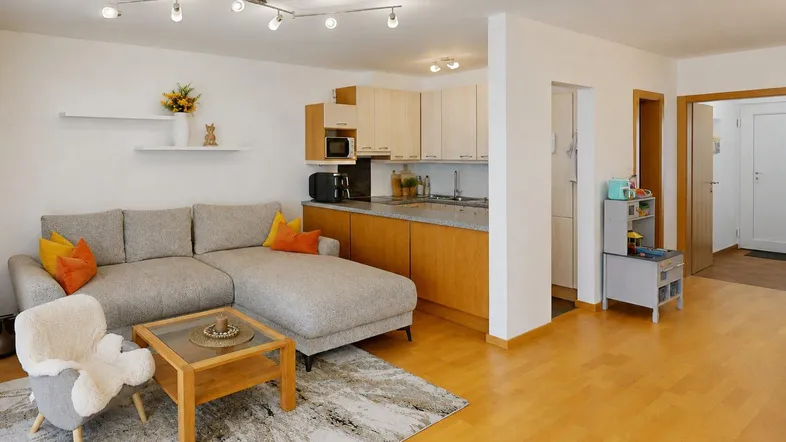 Heller offener Wohnbereich mit integrierter Küche, gemütlichem Sofa und Holzboden.