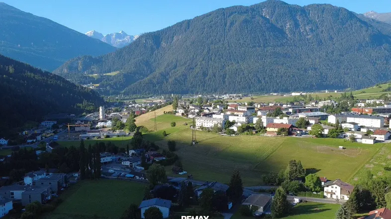 Panoramablick auf ein malerisches Dorf in einem Tal, umgeben von majestätischen Bergen unter blauem Himmel.