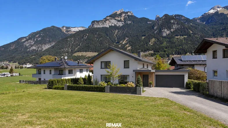 Modernes Einfamilienhaus mit Garage und gepflegtem Vorgarten vor beeindruckender Bergkulisse.