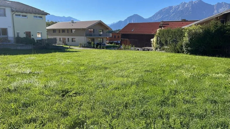 Weitläufige grüne Wiese mit Blick auf umliegende Häuser und majestätische Berge im Hintergrund.