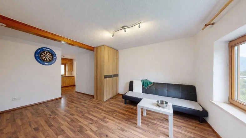 Gemütliches Wohnzimmer mit Laminatboden, Sofa und Blick ins Grüne durch das Fenster.