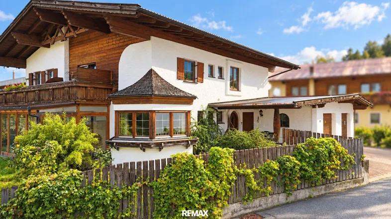 Traditionelles Haus im alpenländischen Stil mit weißer Fassade, Holzbalkonen und gepflegtem Vorgarten.