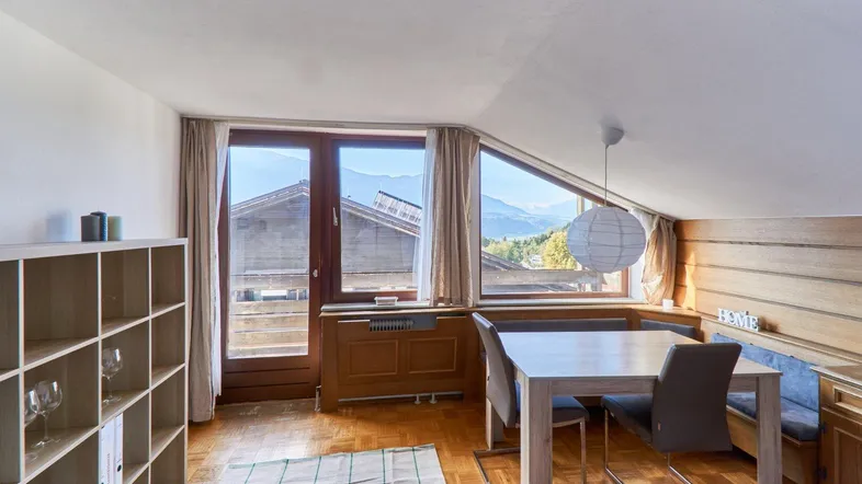 Heller Wohn- und Essbereich mit Holzboden, Dachschräge und Bergblick durch große Fenster.