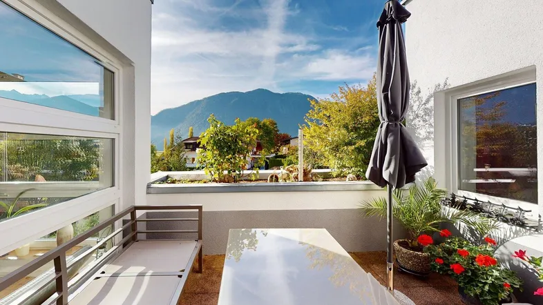 Helle Terrasse mit Bergblick, Gartenmöbeln und Sonnenschirm, ideal zum Entspannen im Freien.