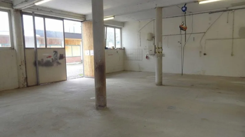 Großer, leerer Innenraum mit Betonboden, Stützpfeilern und großen Fenstern, ideal als Lager oder Werkstatt.