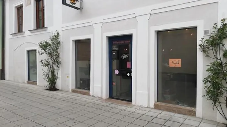 Vorderansicht eines Geschäftsgebäudes mit Schaufenstern und Eingang an einer gepflasterten Straße.
