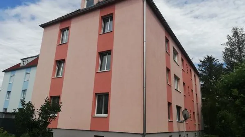Ansicht eines gepflegten Mehrfamilienhauses mit rosafarbenen und beigen Fassaden und Dachgauben.