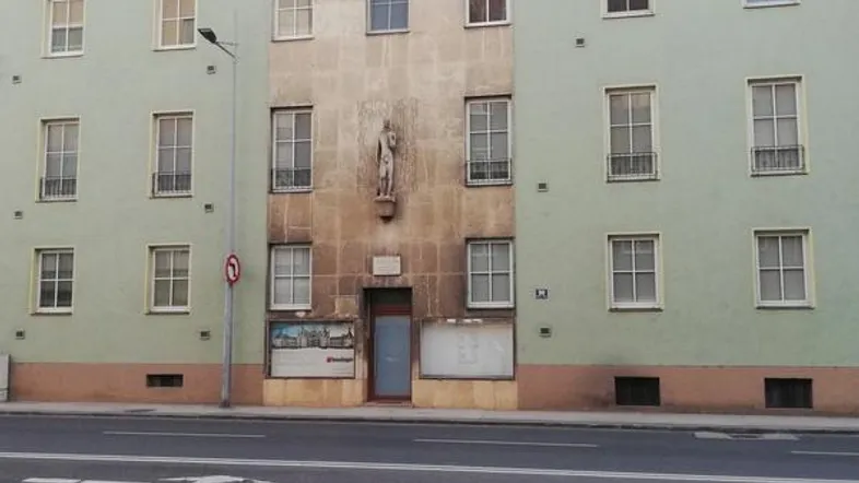 Fassade eines Altbaus mit hellgrüner Farbe, vielen Fenstern und einer zentralen Statue über dem Eingang.