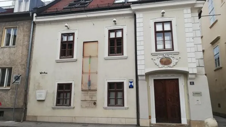 Historisches Gebäude mit klassischer Fassade, braunen Fenstern und rotem Ziegeldach an einer Straße.
