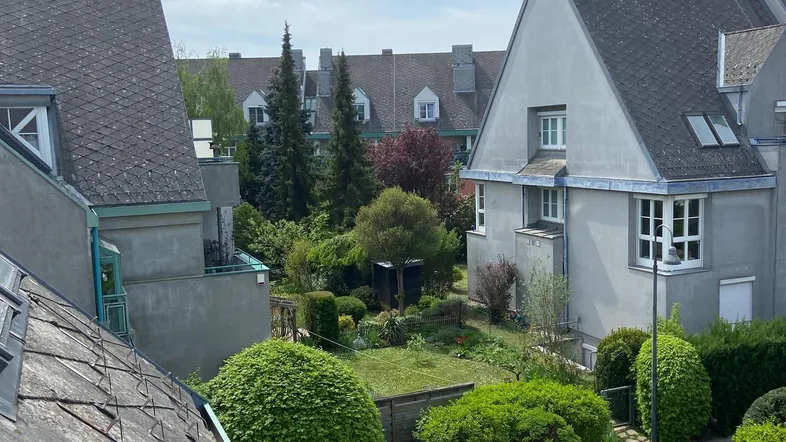 Blick von einem Balkon auf einen gepflegten Gemeinschaftsgarten und umliegende Wohnhäuser.