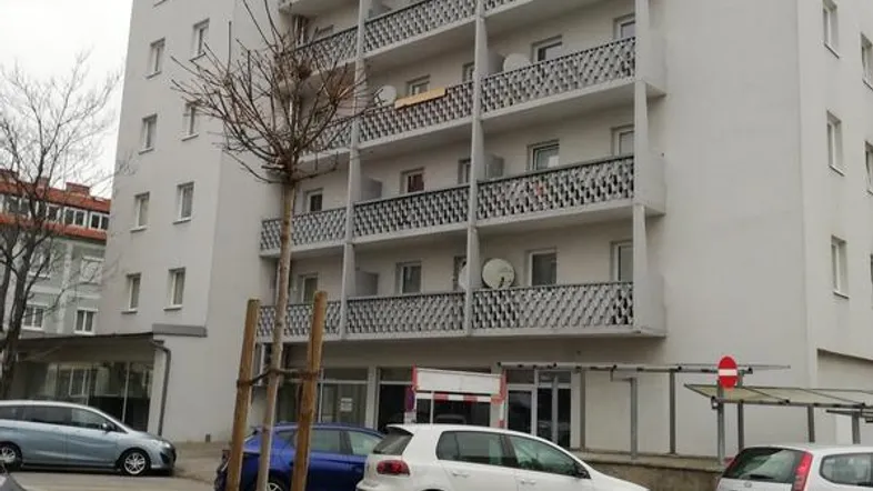 Mehrstöckiges Wohngebäude mit zahlreichen Balkonen und geparkten Autos davor.