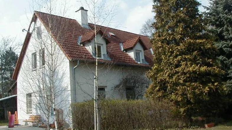 Weißes Einfamilienhaus mit rotem Satteldach, Dachgauben und umgebender Grünfläche mit Spielbereich.