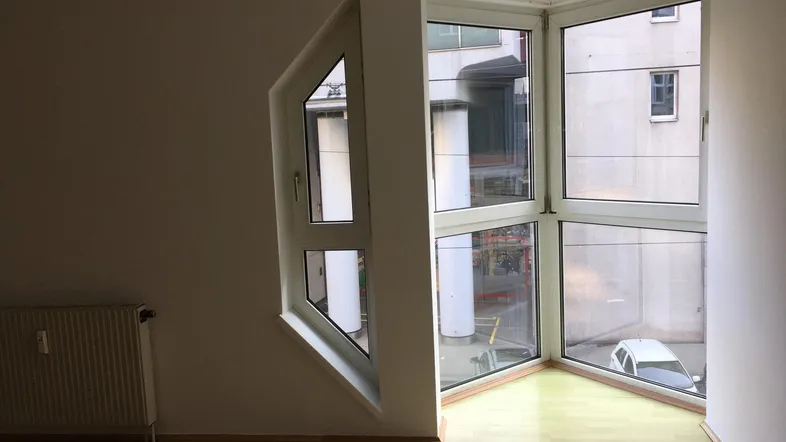 Heller Raum mit Parkettboden, Heizkörper und einer einzigartigen Eckfensterfront, die viel Licht hereinlässt.