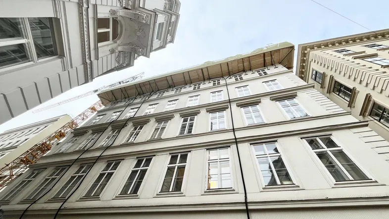 Blick auf die Fassade eines Altbaus mit vielen Fenstern und Bauarbeiten am Dachgeschoss.